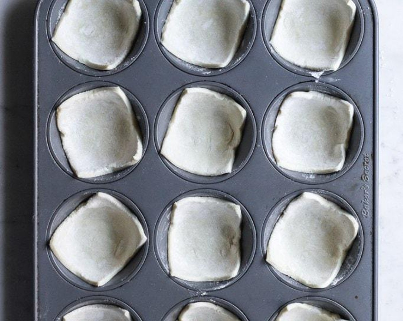 step 4 Taking one square of puff pastry at a time, slightly stretch it with your hands into a square & place into the well of a muffin pan. Repeat with all squares.