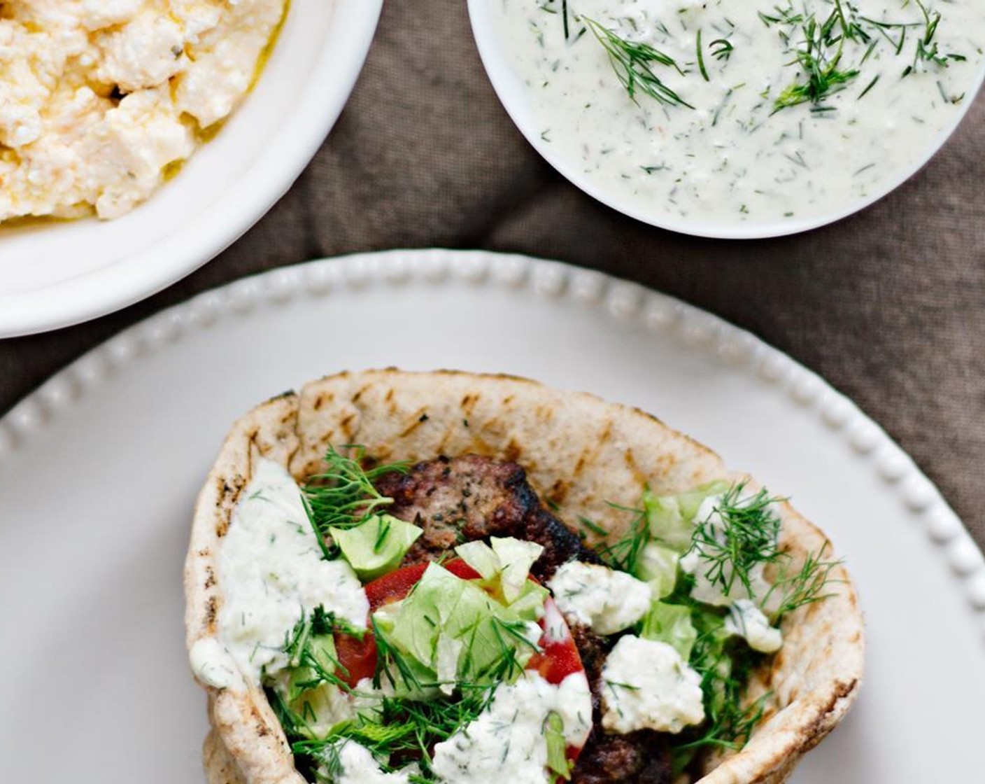 step 15 To build the burgers, place a lamb patty on the center of each pita. Cover with sliced tomatoes, shredded lettuce, the reserved dill, and a couple dollops of tzatziki or tirokafteri. Add Hot Sauce (to taste), if so desired.