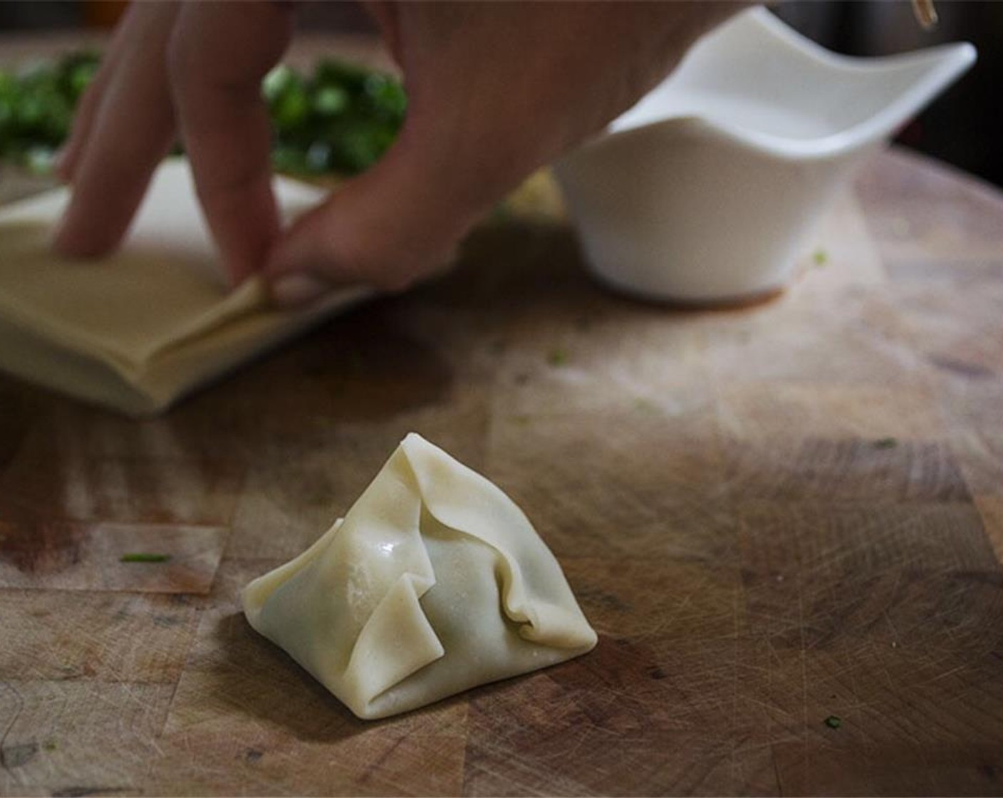 step 9 Spoon 1 tbsp. filling in the center of one of the Wonton Wrappers (15). Dip an index finger in a dish of water. Brush the outer edges around the filling. Fold the opposite corners together two at a time. Pinch to seal the wonton together. Fold corners over as you go. Repeat.