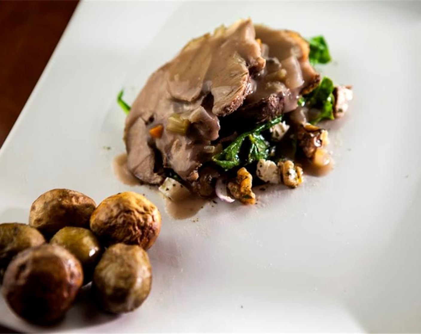 step 14 Slice the roasted leg of lamb into thin slices. Plate the dish by laying the slice on top of the salad, and spooning some of the sauce on top. Serve with roasted mushrooms and Brussels sprouts on the side.