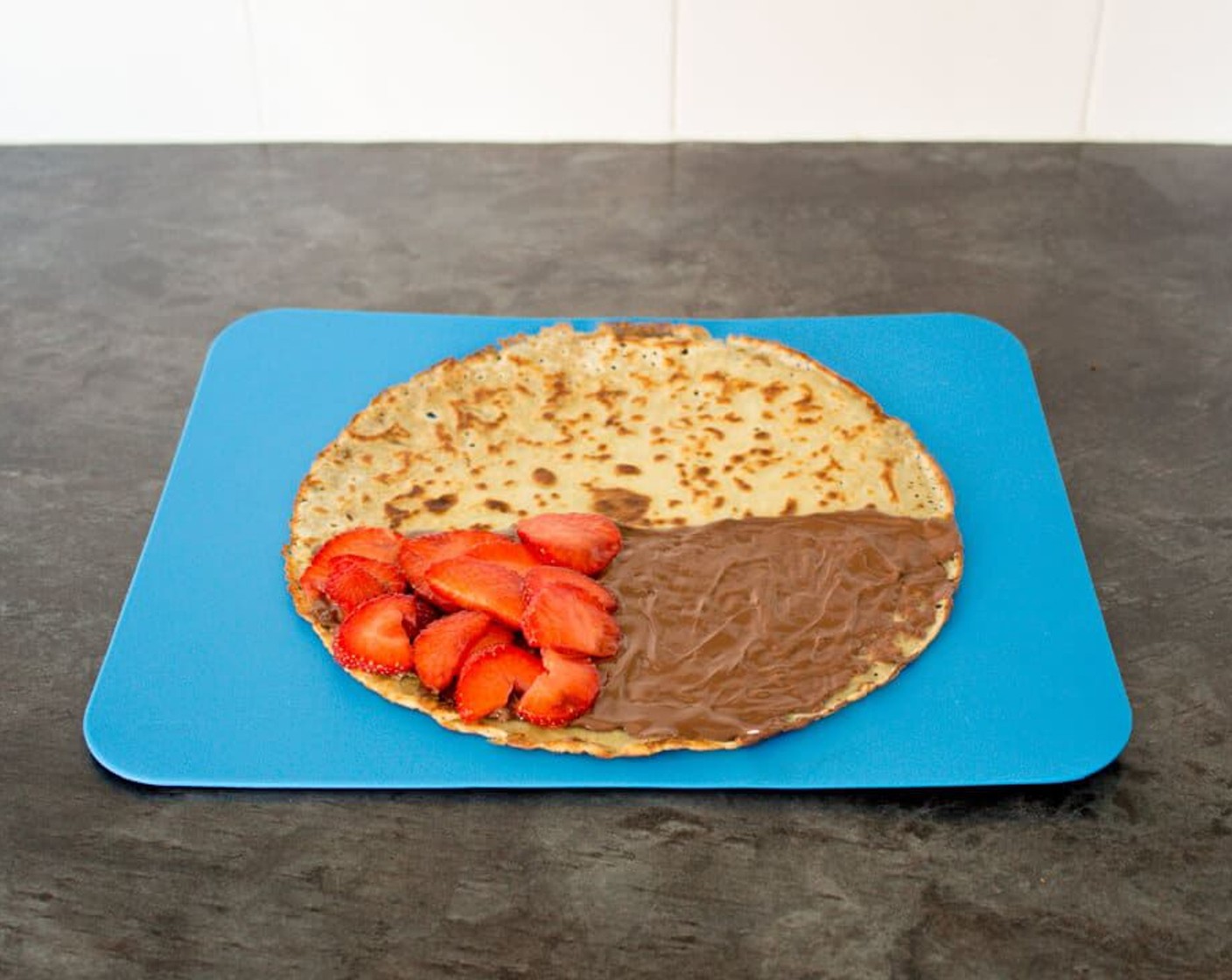 step 9 Slide the crepe out the pan and onto a chopping board or mat. Smear half the crepe with warmed Nutella or Biscoff. Top a quarter of the Nutella/Biscoff half with sliced strawberries.