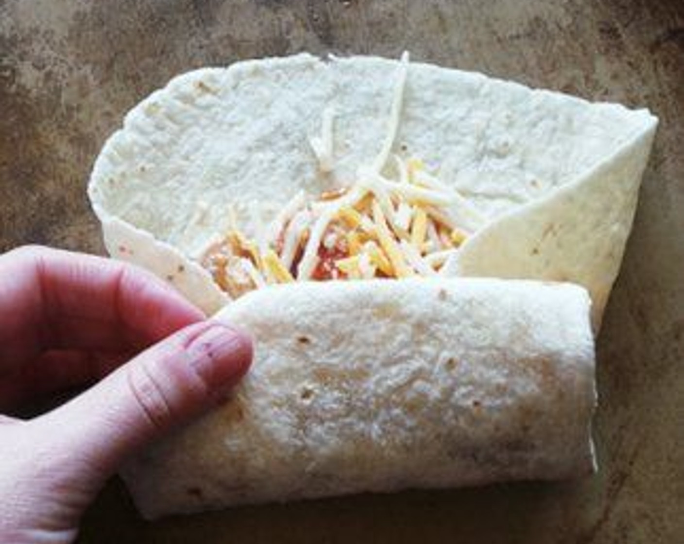 step 5 Spread a spoonful of beans on the tortilla, then top with chicken and cheese. Fold ends in, then turn tortilla to wrap. Lay each on a baking sheet.