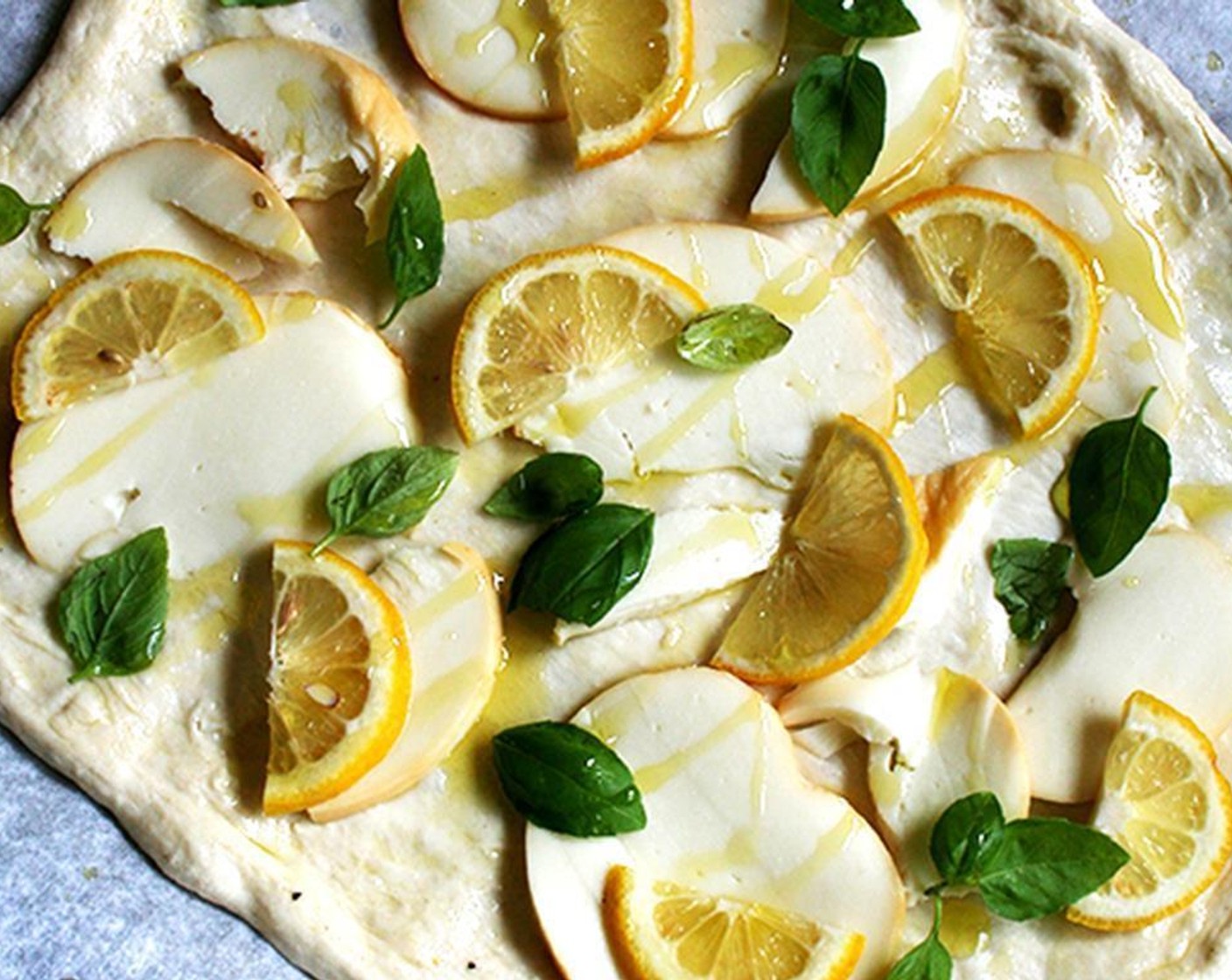 step 4 Distribute 3 ounces of cheese over the surface, leaving a 1-inch rim. Arrange the lemon over the cheese and tuck in the Fresh Basil Leaves (5) then drizzle everything lightly with Extra-Virgin Olive Oil (as needed), including the rim of the crust.