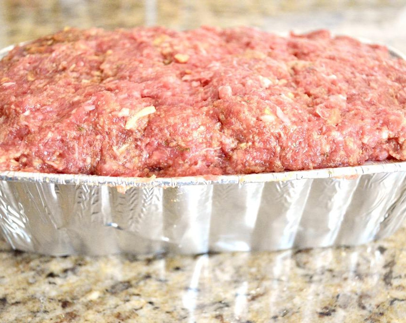 step 2 Get a loaf pan, and combine the Ground Beef (2 lb), Seasoned Breadcrumbs (2/3 cup), Onion Soup and Dip Mix (1 packet), Eggs (2), McCormick® Garlic Powder (1 pinch), Salt (1 pinch), and Freshly Ground Black Pepper (1 pinch) in a bowl and use your clean hands to thoroughly mix it together. Press the mixture firmly into the loaf pan and put the full loaf pan on the sheet tray.
