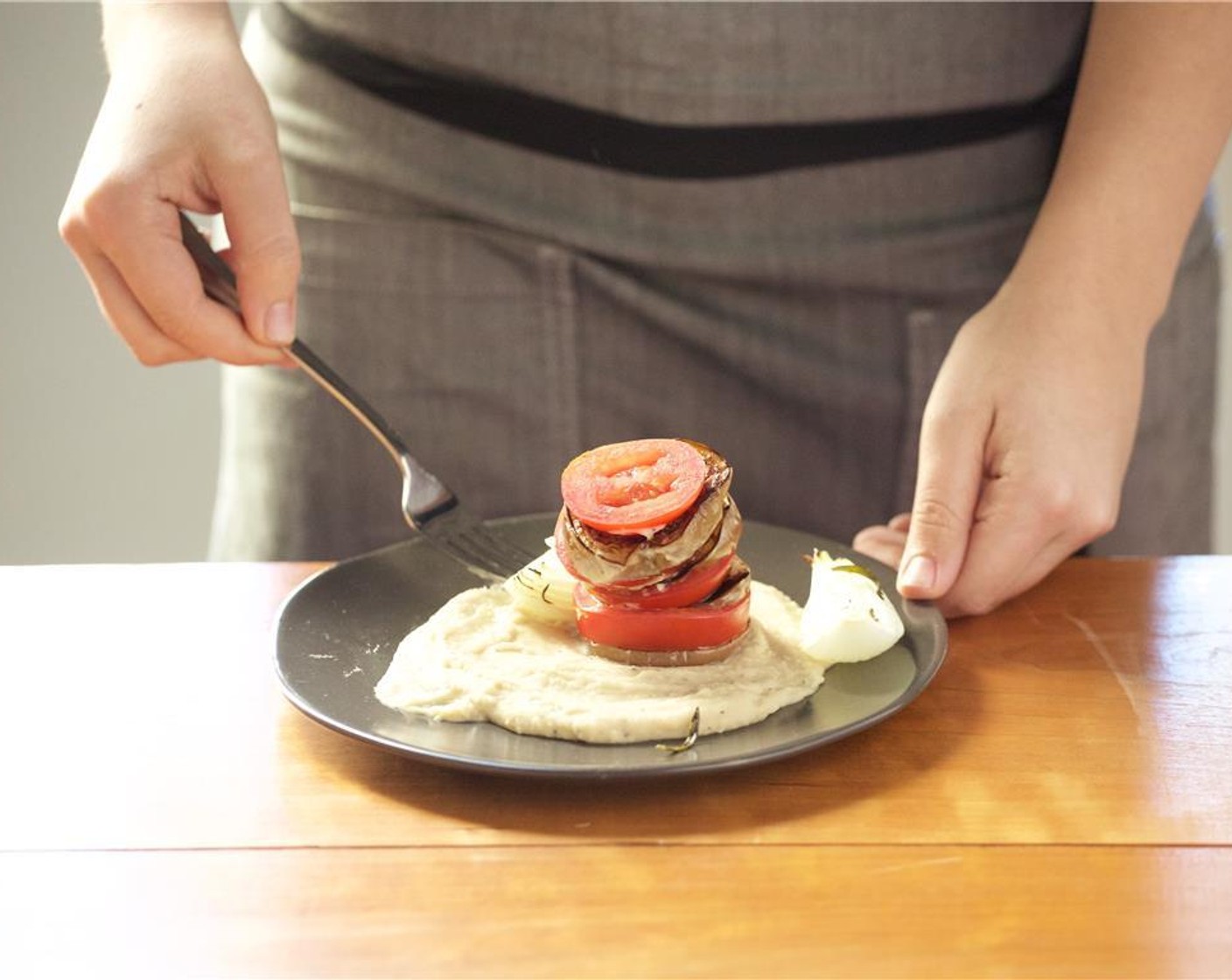 step 9 In the center of two plates evenly distribute the mashed cannelini beans. Stack a tower on each plate of tomato and eggplant pieces. Serve the roasted onion on the side.