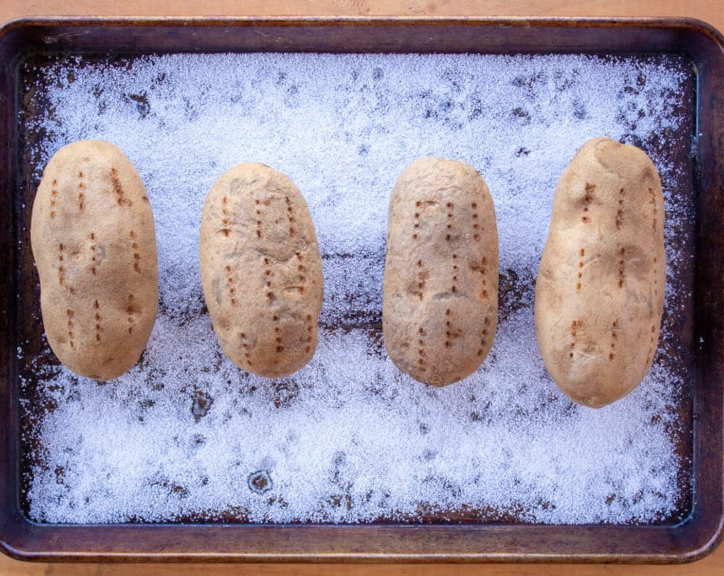 step 2 Cover a baking sheet with Kosher Salt (1/2 cup) and place the Russet Potatoes (2 lb) on top. Pierce them all over with a fork and put them in the oven to bake for 1 hour and 10 minutes.