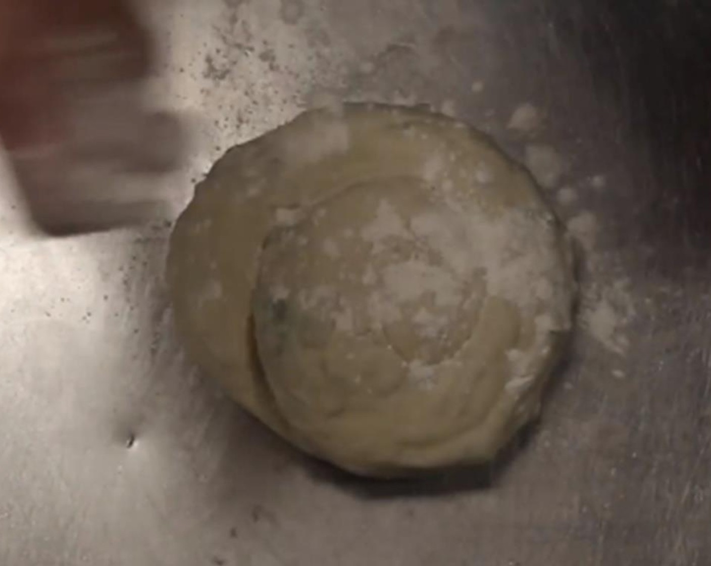 step 12 Continue to coil the dough to create the shape of a cinnamon bun. Take the loose end and tuck it under the bun. Then push down on the dough to begin to flatten the bun into a circle pancake.