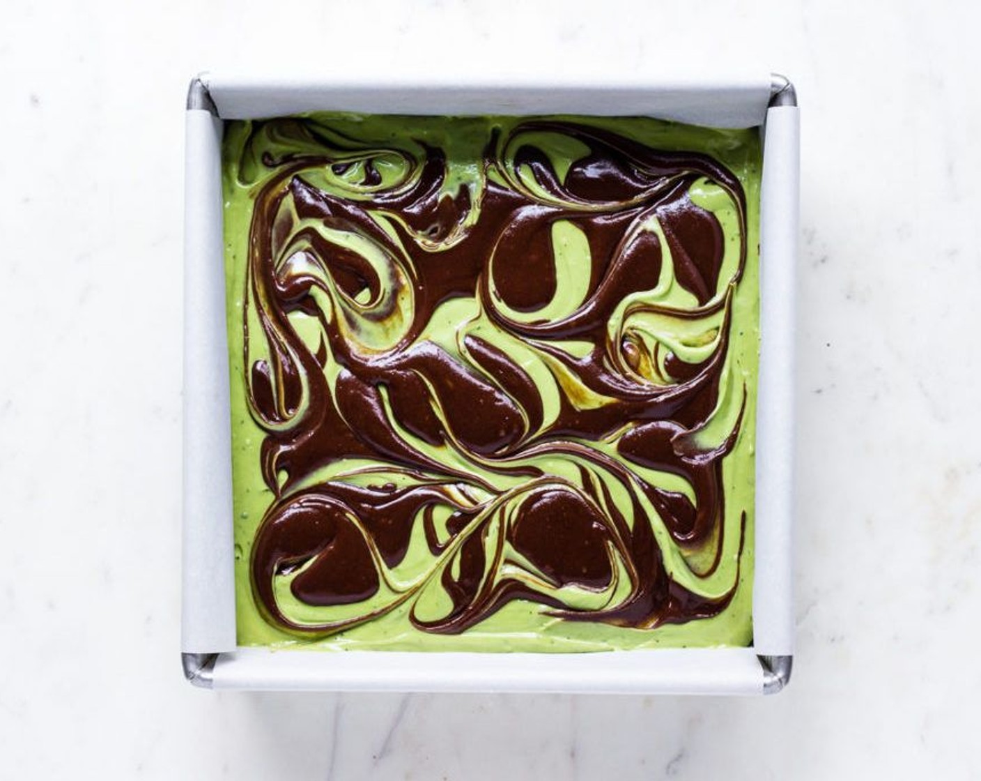 step 7 Add the remaining 1/4 of the brownie batter to the top of the matcha cheesecake layer in tablespoon dollops. Use the tip of a paring knife to swirl the brownie batter and matcha cheesecake into a marbled pattern.