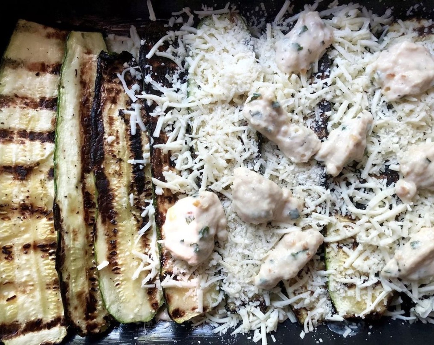 step 8 To assemble the casserole, start off by spreading a third, about 2/3 cup, of the sauce on the bottom of the prepared baking dish. Next, add a layer of zucchini strips with the grilled sides facing up. Then sprinkle half of the Shredded Mozzarella Cheese (115 g) and half of the Grated Parmesan Cheese (30 g) over the entire surface.