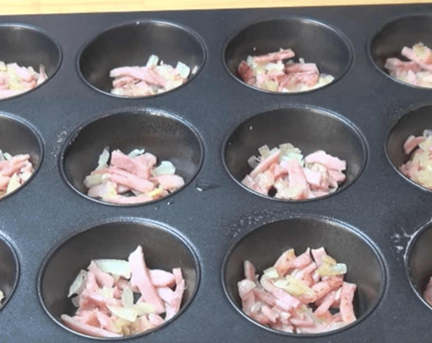 step 2 Lightly grease a muffin pan with some Oil (as needed) and divide the ham and onion mixture between each of the holes.