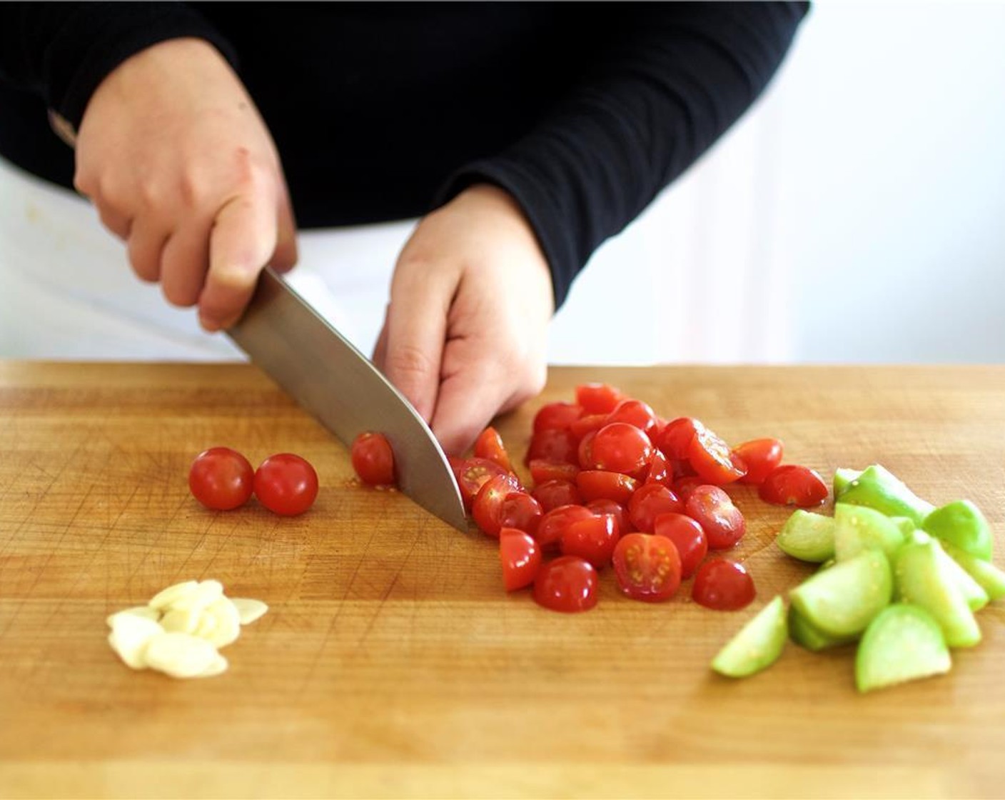 step 2 Slice the garlic lengthwise, and set aside. Cut the Tomatillos (2) into eight wedges each, then set aside. Slice the Cherry Tomato (1 cup) in half, and set aside. In a large saute pan, heat four cups of water over high heat and bring to a boil.