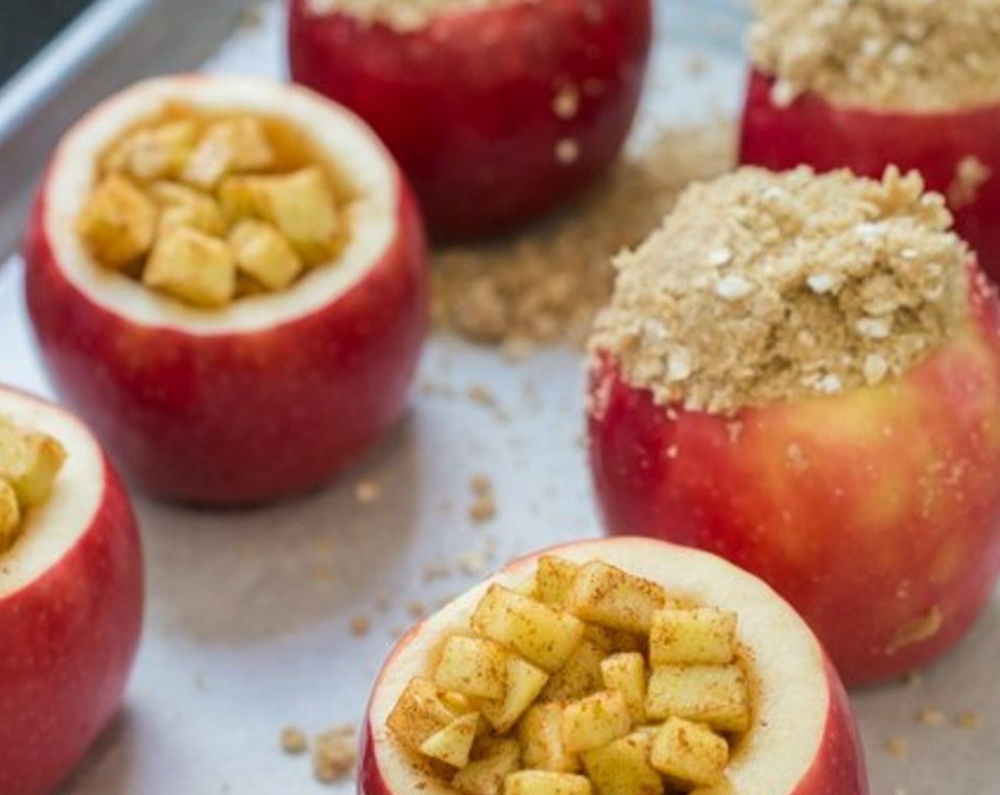 step 7 Line a baking sheet with parchment paper. Arrange the red apples on the baking sheet. Fill the red apples with the diced green apple, then top them with the crispy topping mixture.