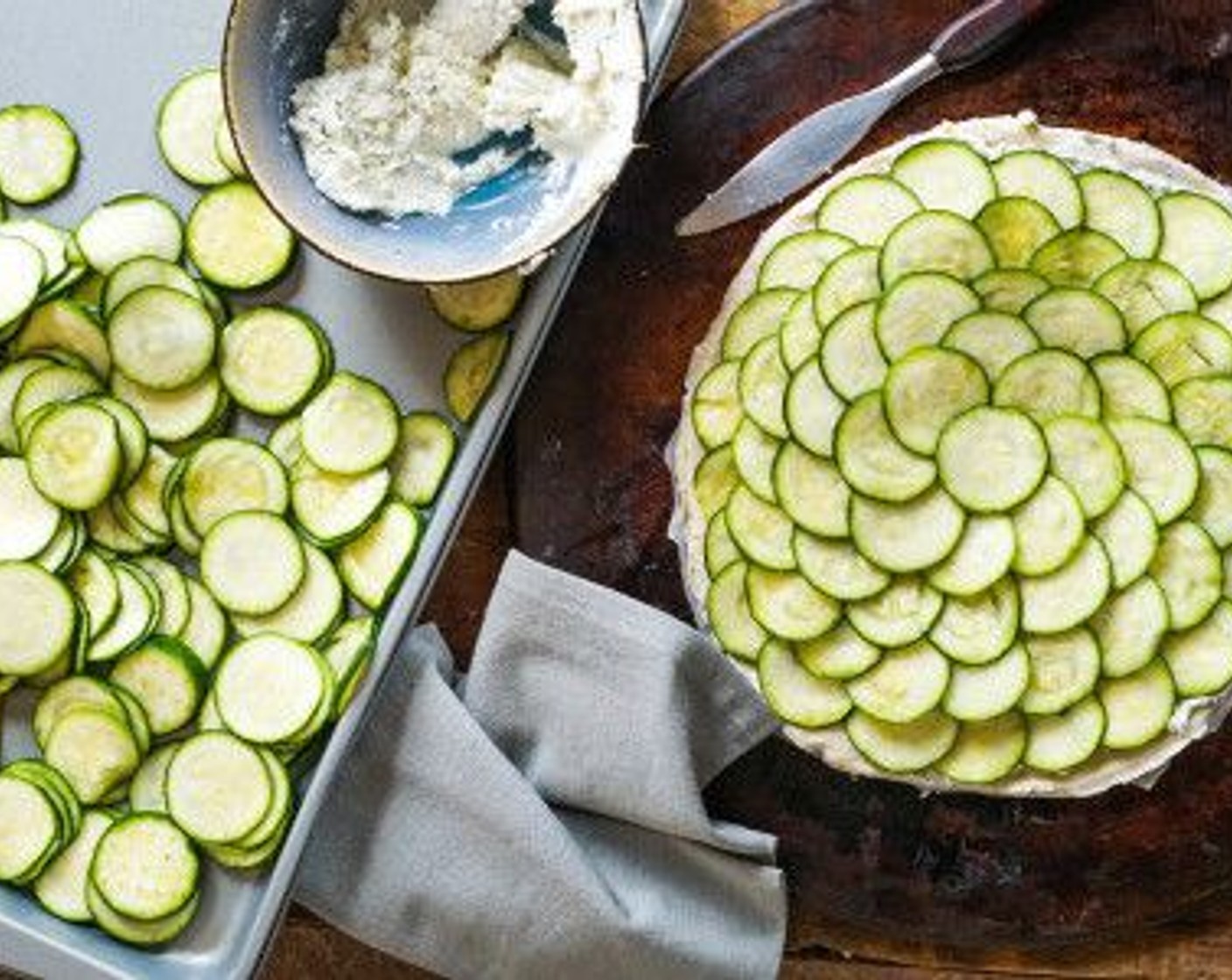 step 10 Lay the zucchini slices in overlapping circles, starting at the very edge of the cheese and working your way to the center. Once the whole tart is covered, drizzle with more olive oil, and sprinkle once more with pepper.