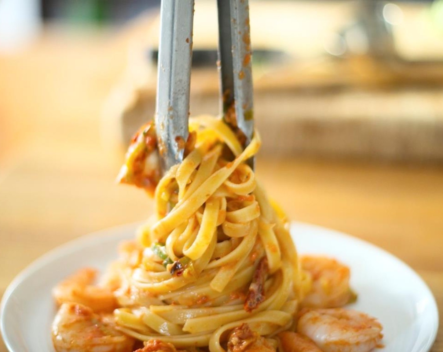 step 14 Place the shrimp evenly between two plates in a single circular layer centered on the plate. Reserve four shrimp for garnish. Using tongs, grab a single portion of pasta. Twirl pasta around the tongs and then center it with height over the shrimp.