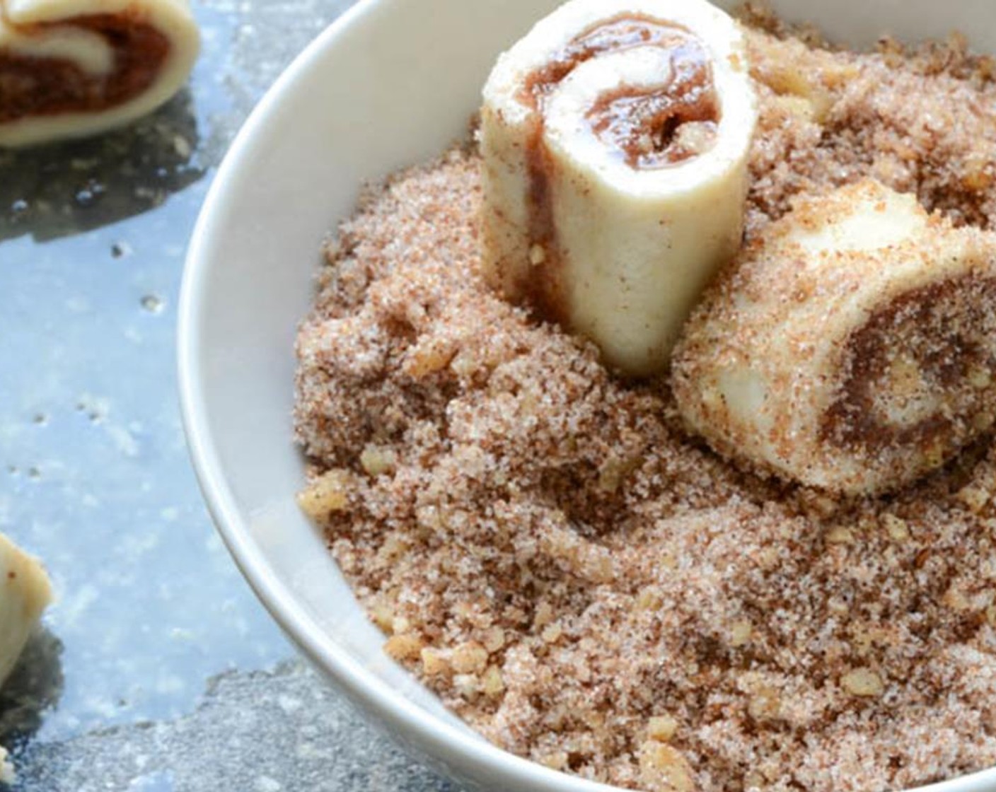 step 16 Use a serrated knife to cut the roll into 1" slices. Toss each slice in the cinnamon sugar mixture, lightly pressing the coating and nuts into the cookie.