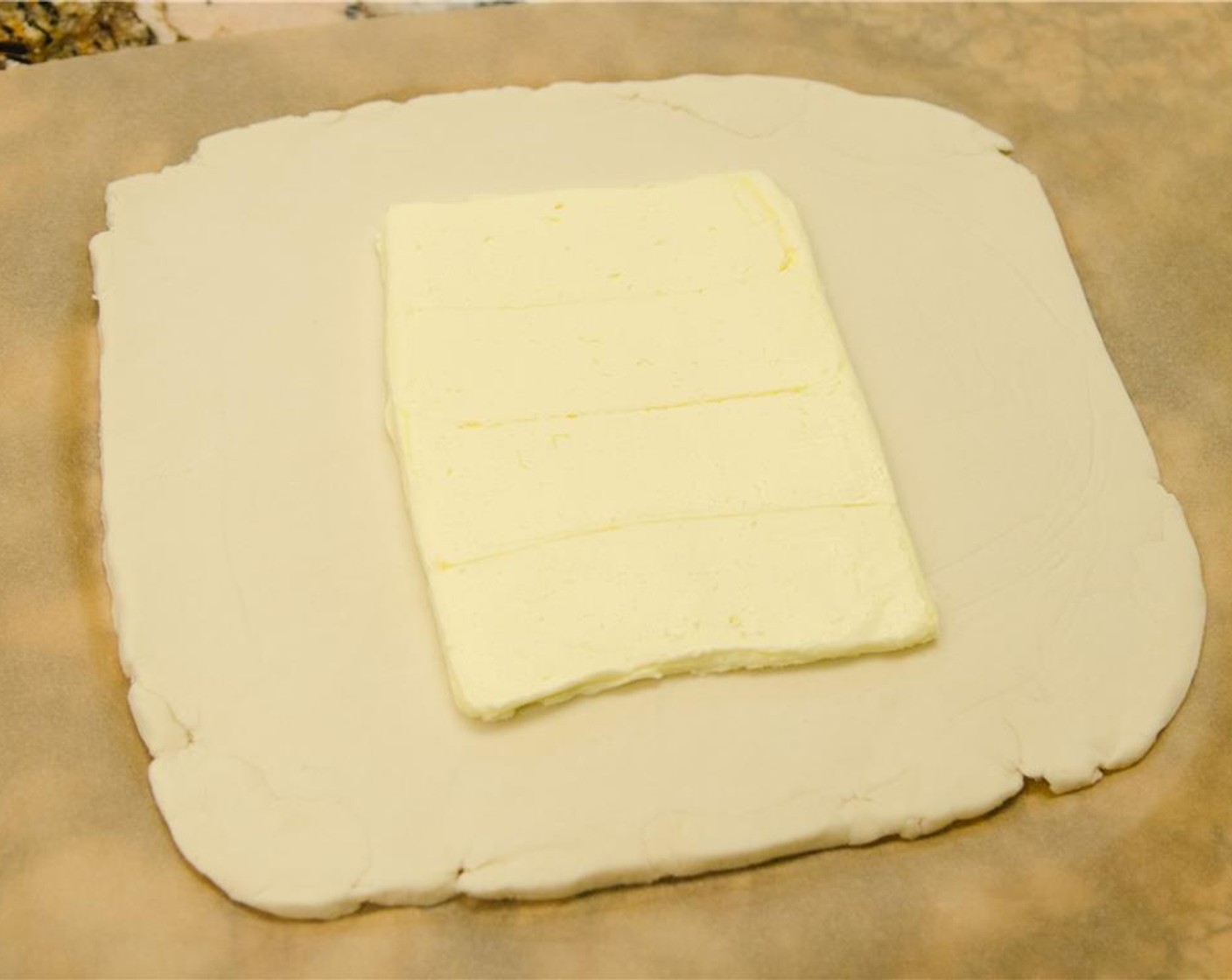 step 7 Remove the top layer of plastic or parchment from the dough and unwrap the butter block.  Place the butter block in the center of the dough square.