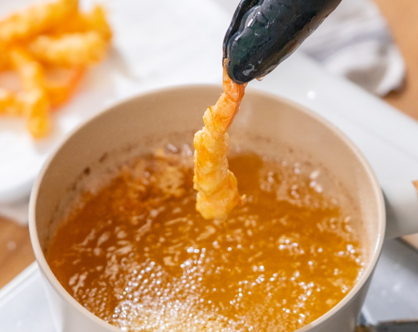 step 9 Coat the prawns evenly with batter. Pick up the prawns from the tail part and let the excess drip off for a second. Then gently place it into the hot oil. Fry for about 1 minute. Transfer the shrimp to a wire rack or a tray lined with paper towels to drain the excess oil.