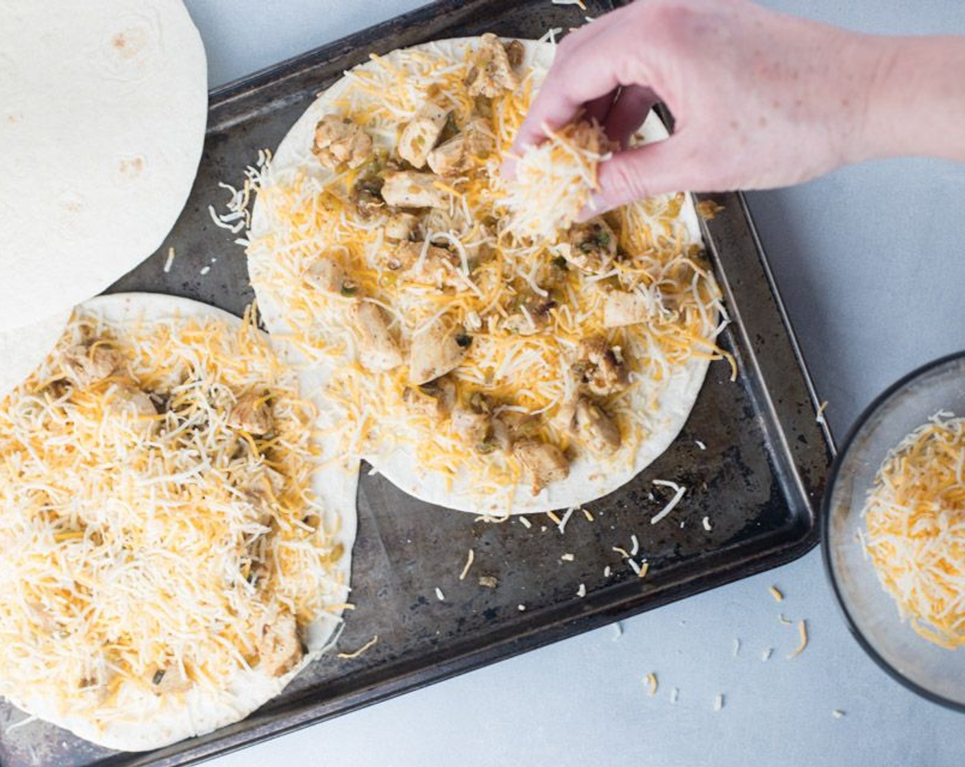 step 5 On a sheet pan, lay one Flour Tortillas (4) down and spread about one fourth of the Shredded Mexican Cheese Blend (3 cups) on the tortilla. Next, continue with a layer of half of the chicken filling. Finish off tortilla with another layer of cheese.