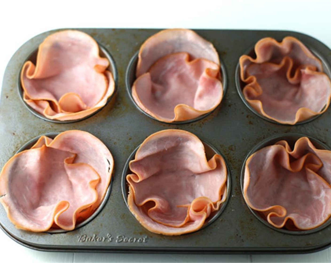 step 2 Place 2 slices of Applewood Smoked Ham (12 slices) in each muffin cup, pressing down in the middle to make room for the egg. Crack one Eggs (6) into each ham cup.