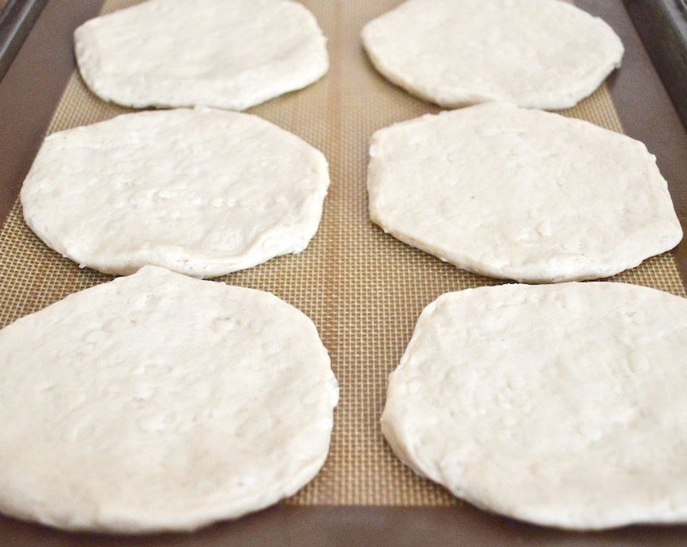 step 5 While the mixture simmers, take each Pillsbury Grands!™ Southern Style Biscuits (16) and lay them out on the lined sheet trays. Press them down firmly into thin discs and stretch them out a little.