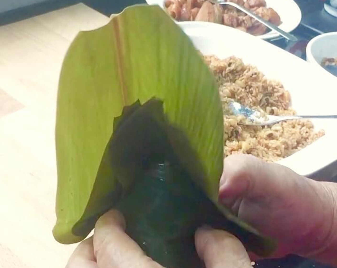 step 34 Next, fold the leaves over to cover the open top of the rice dumpling completely. Make sure you press the tip of the rice dumpling so that the end is pointed. Then fold the leaves over the edges of the cone in a triangular shape.