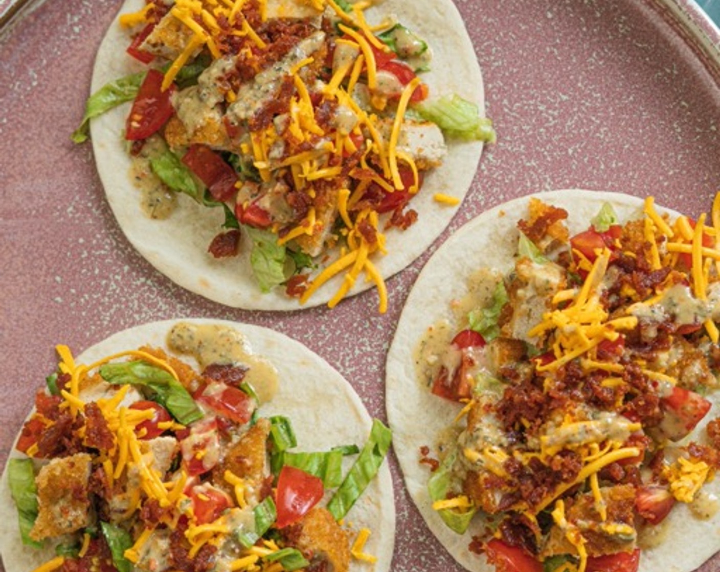 step 2 Top tortillas with Vegan Chicken Strips (2 1/2 cups), Vegan Cheddar Cheese (1 cup), Roma Tomatoes (2), Vegan Bacon (8 slices), Lettuce (1 1/2 cups), and drizzle with Vegan Ranch Dressing (1/4 cup).