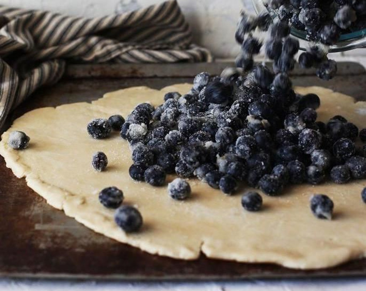 step 5 Roll out the dough into a 12-inch circle, adding more flour to the surface when needed. Transfer the dough onto a baking sheet or pizza stone. Dump the blueberry mixture in the center of the circle leaving a 2-inch margin around the edges.