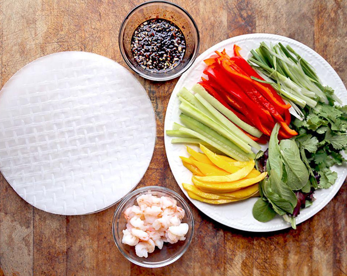 step 4 Put the rice paper on the towel and place a couple of Red Bell Pepper (1) slices, English Cucumber (1/2), the green part of the Scallions, Mango (1), Fresh Cilantro (1 cup) leaves, Lettuce (1 cup) leaves and Large Shrimp (12). Place the ingredients off-center, towards one side of the rice paper wrapper.