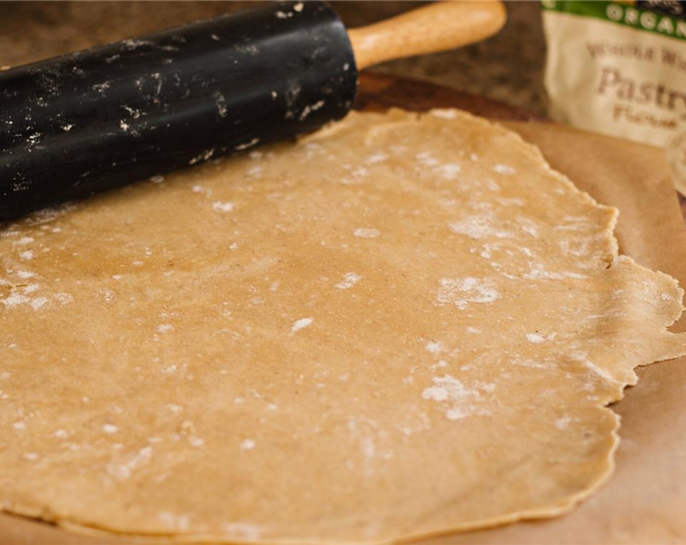 step 11 Remove the dough from the fridge. Sprinkle a piece of parchment with whole wheat pastry flour, and sprinkle the top of the dough with flour. Use a rolling pin, bottle of wine, or glass to flatten the dough into a 1/4 inch-1/8 inch circular crust.