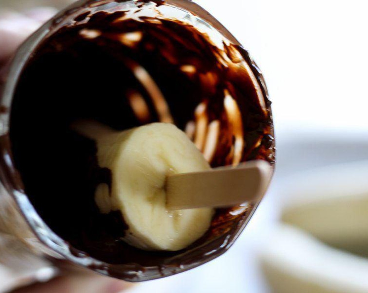 step 4 Tilt the glass toward you, and carefully roll and twist the banana pop until it is evenly covered in dark chocolate.