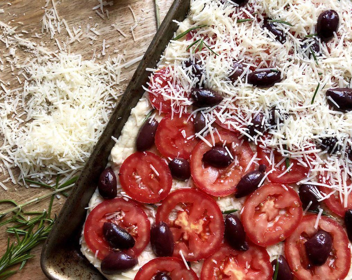 step 5 Brush the top of the dough generously with Extra-Virgin Olive Oil (as needed).  Sprinkle with half of the Asiago Cheese (2/3 cup) and Rosemary Leaves (1/2 Tbsp). Arrange the Plum Tomatoes (3) in a single layer on top of the cheese. Place the Kalamata Olives (1/2 cup) evenly over the tomato slices.