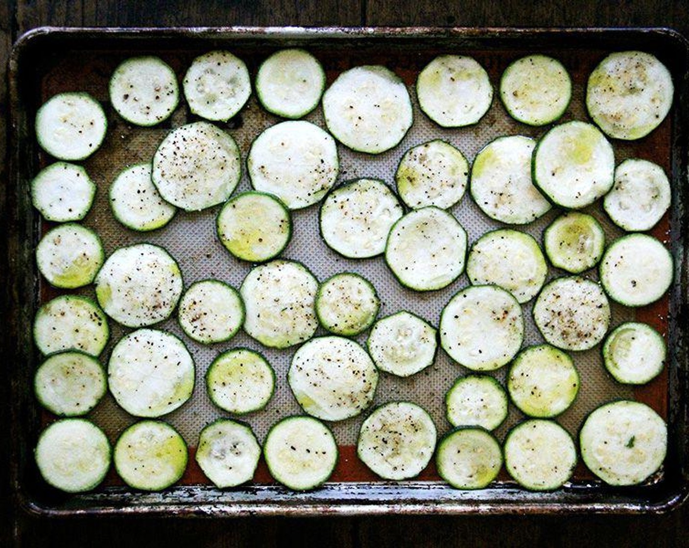 step 2 Arrange the Zucchini (905 g) in single layers on two Silat or parchment-lined rimmed sheet pans. Season with Kosher Salt (to taste) and Freshly Ground Black Pepper (to taste) on each side, drizzle each pan with Extra-Virgin Olive Oil (2 Tbsp), toss to coat, then spread into an even layer.