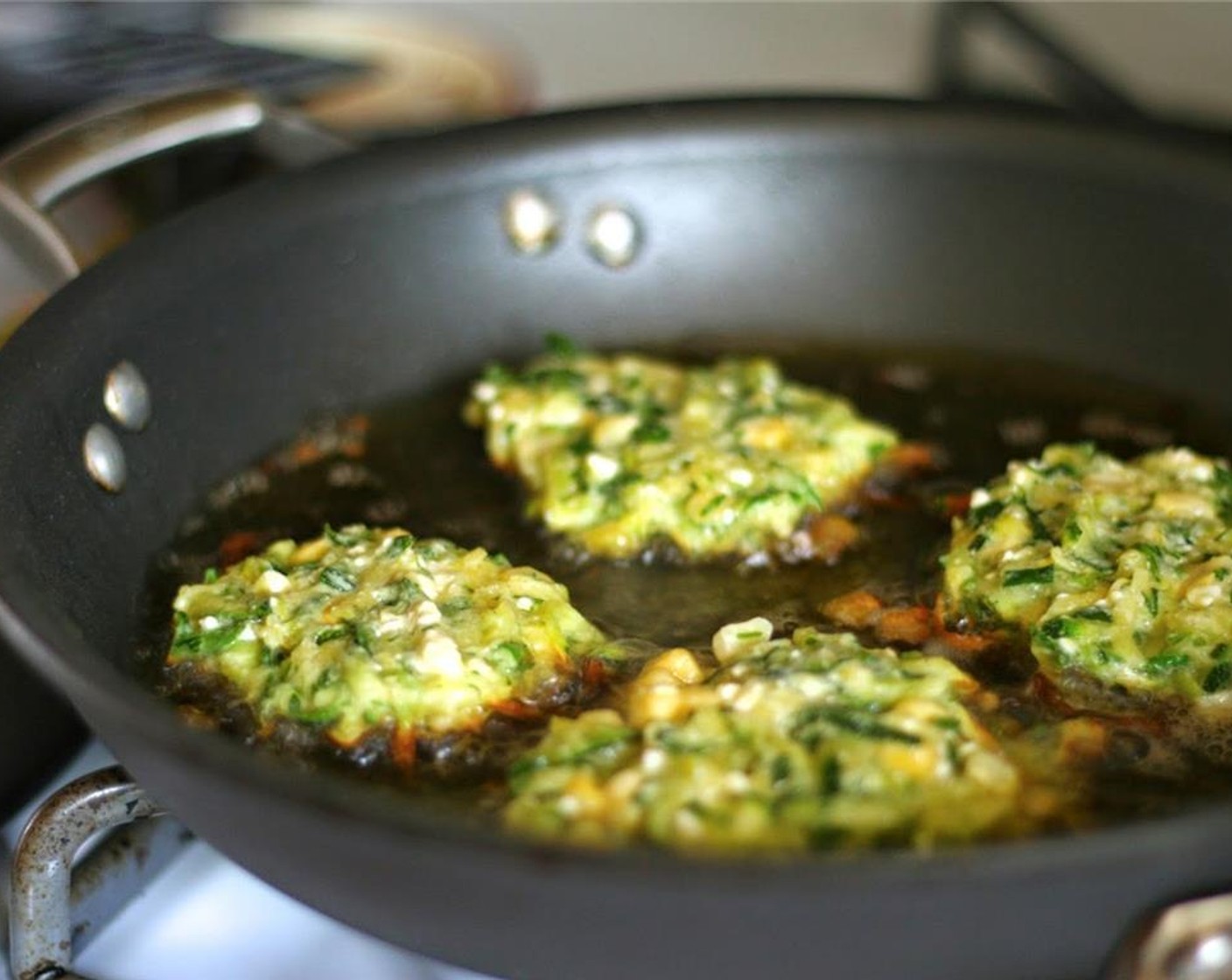 step 5 Place Extra-Virgin Olive Oil (as needed) in a pan and heat medium-high. Working in batches, take small scoops of the zucchini mixture, place mounds in hot oil, and lightly pat down with a spatula. Fry until golden brown on the outside.