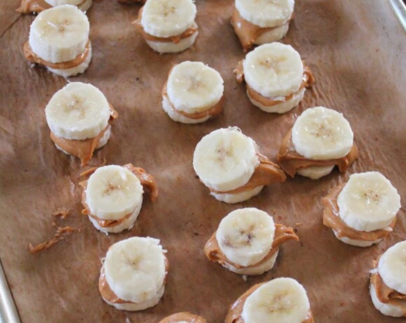 step 1 Place Bananas (3) on a baking tray. Spoon out about 1/2 tablespoon of Peanut Butter (1/2 cup) on each. Place another slice of banana over the peanut butter to sandwich together. Repeat.