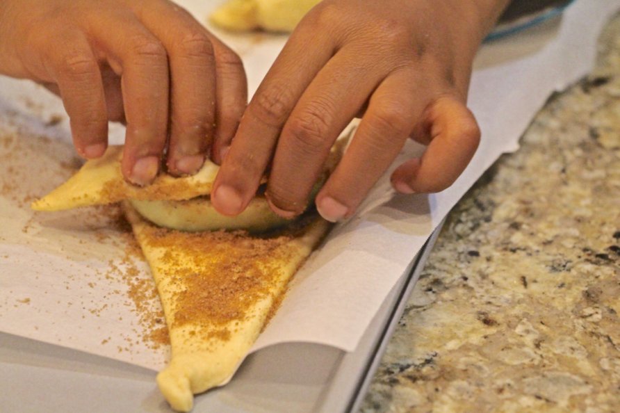 Step 7 of Apple Pie Bites Recipe: Starting at the wide end of each triangle, roll the apple in the crescent dough.