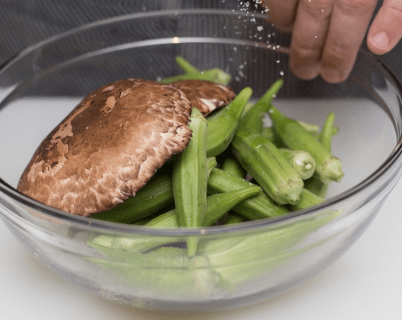 step 4 Place Okra (to taste) and mushrooms in a large mixing bowl. Drizzle with Olive Oil (1/2 Tbsp) and Kosher Salt (1/2 tsp) to bowl and mix thoroughly. Carefully remove baking pan from oven.