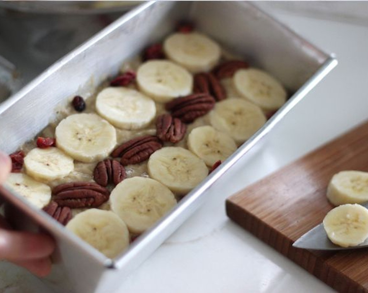 step 9 Cut Banana (1) into slices and put them on top of the banana bread. You can also add Pecans (to taste) and Dried Cranberries (to taste) if you like.