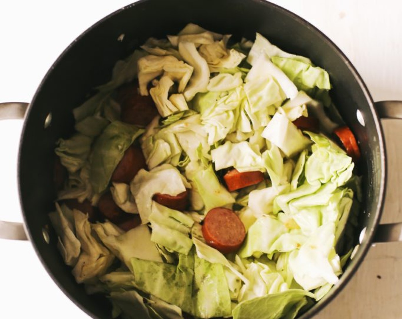 step 4 Stir in the Green Cabbage (1/2 head) and toss so it coats in the sausage, onions, and oil. Add 2 additional Tbsp of Butter (as needed), reduce heat to medium-low, and cover the pot halfway. Allow it to cook for 15-20 minutes, stirring every 5 minutes until the cabbage is wilted and tender. Season with a few pinches of each Salt (to taste) and Ground Black Pepper (to taste).