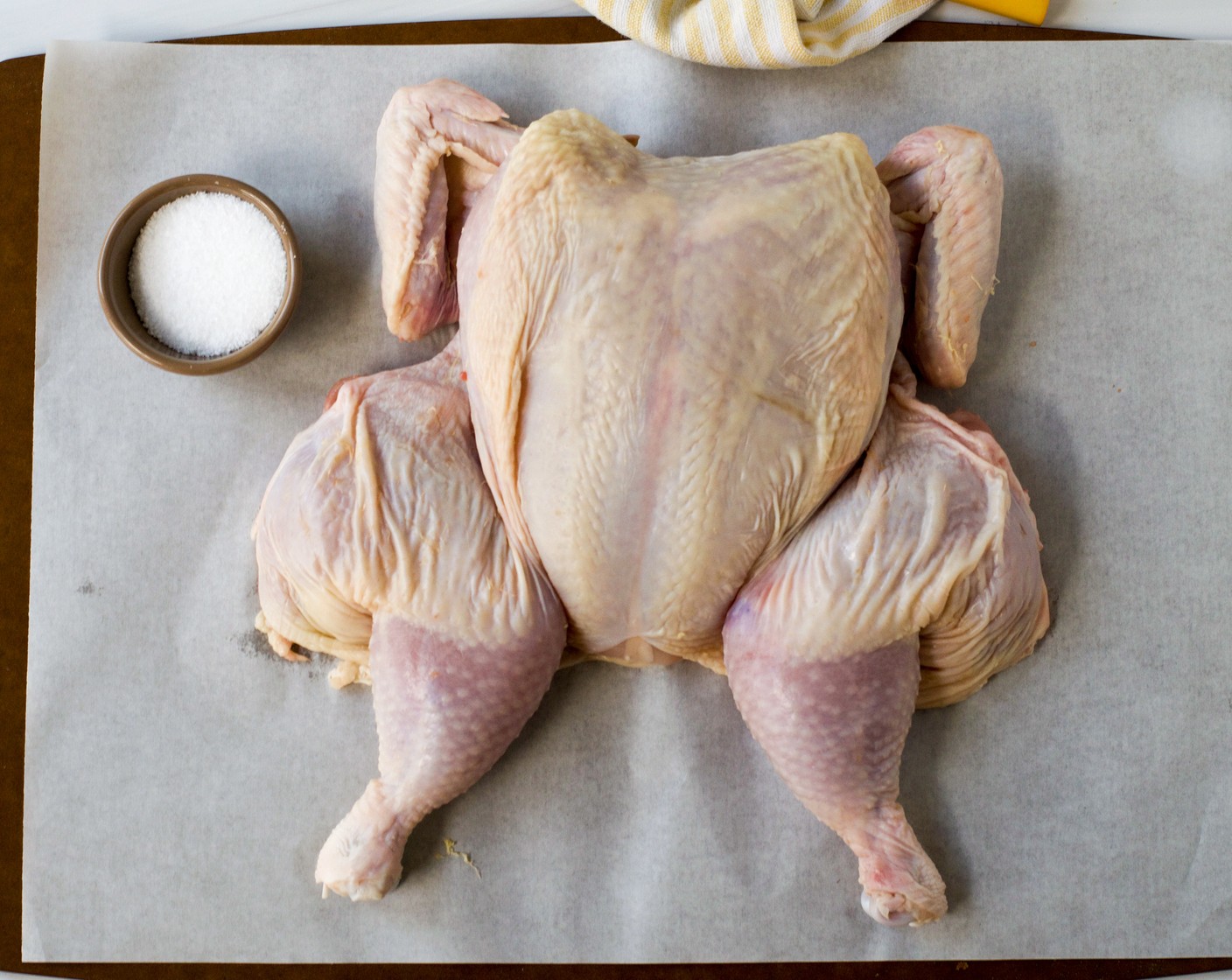 step 3 Spatchcock the Whole Chicken (1): Turn the chicken breast side down on a cutting board. Using kitchen shears, cut along one side of the backbone from back to front. Then cut along the other side and remove the backbone. Turn the chicken over and with the palm of your hand, press down on the breastbone until you feel it crack. Turn the legs out and tuck the wing tips under the breast so that the chicken lies flat.