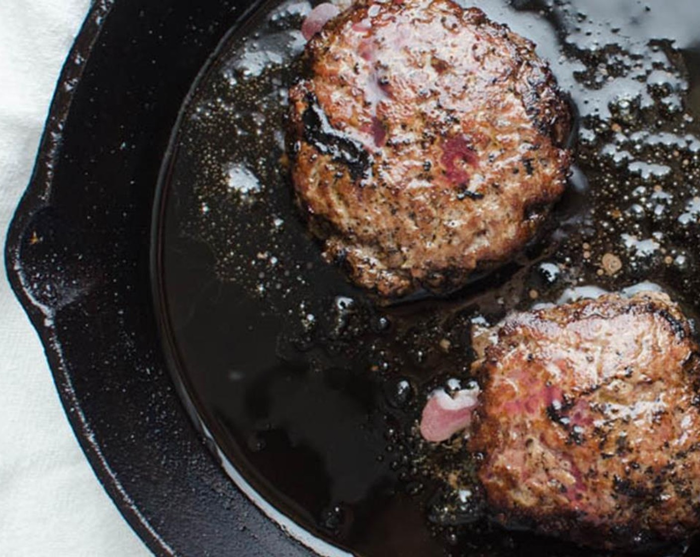 step 10 Working in batches, heat the cast iron skillet over medium high heat and when the bacon fat is good and hot, carefully place a few meat balls into the pan. Use a spatula or burger press to flatten the burger to about a half-inch thick.  Do this for each of the burgers in the pan.