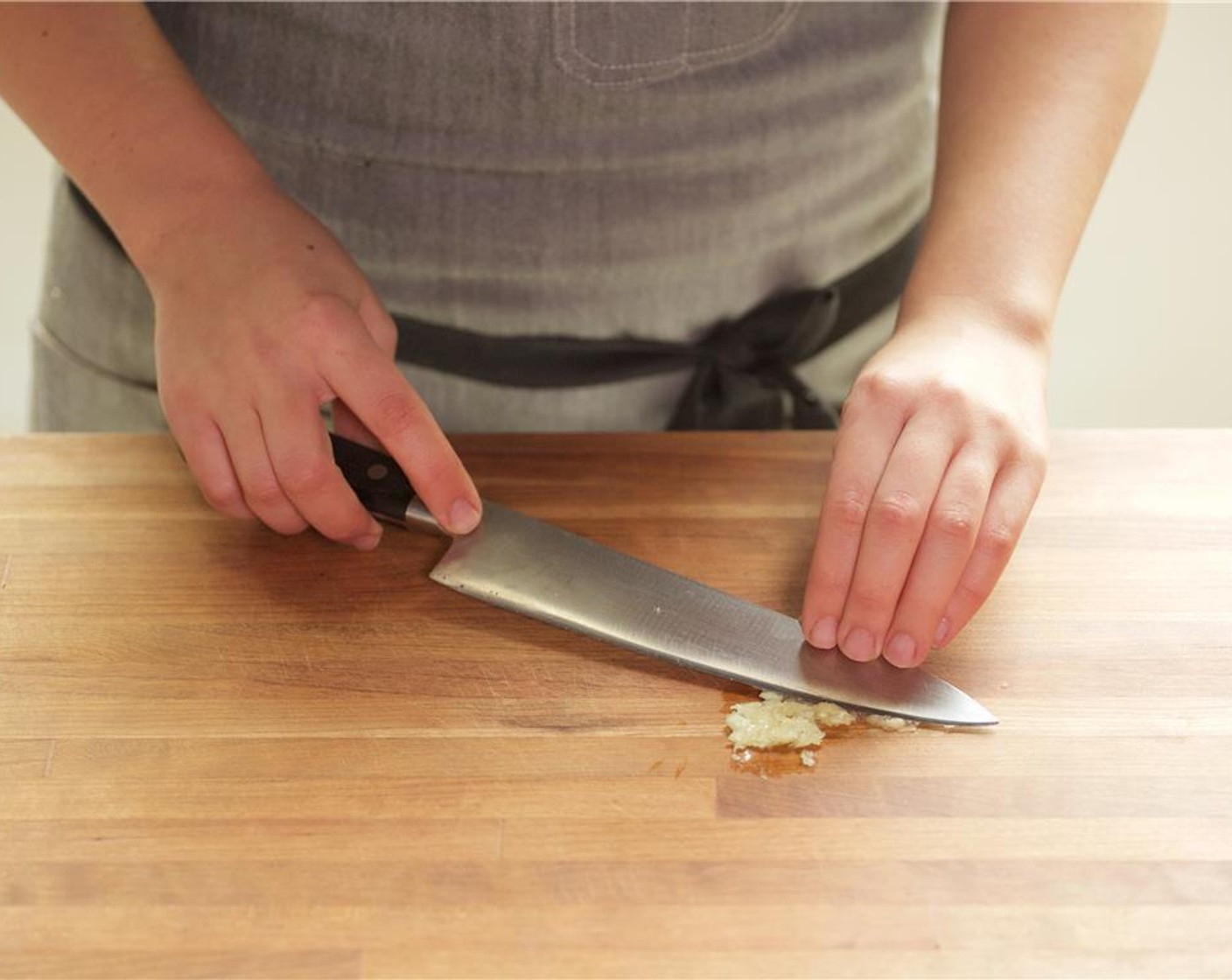 step 3 Tilt the knife at an angle and drag it over the garlic, scraping it across the surface of the board until the garlic becomes a smooth paste. Set aside.