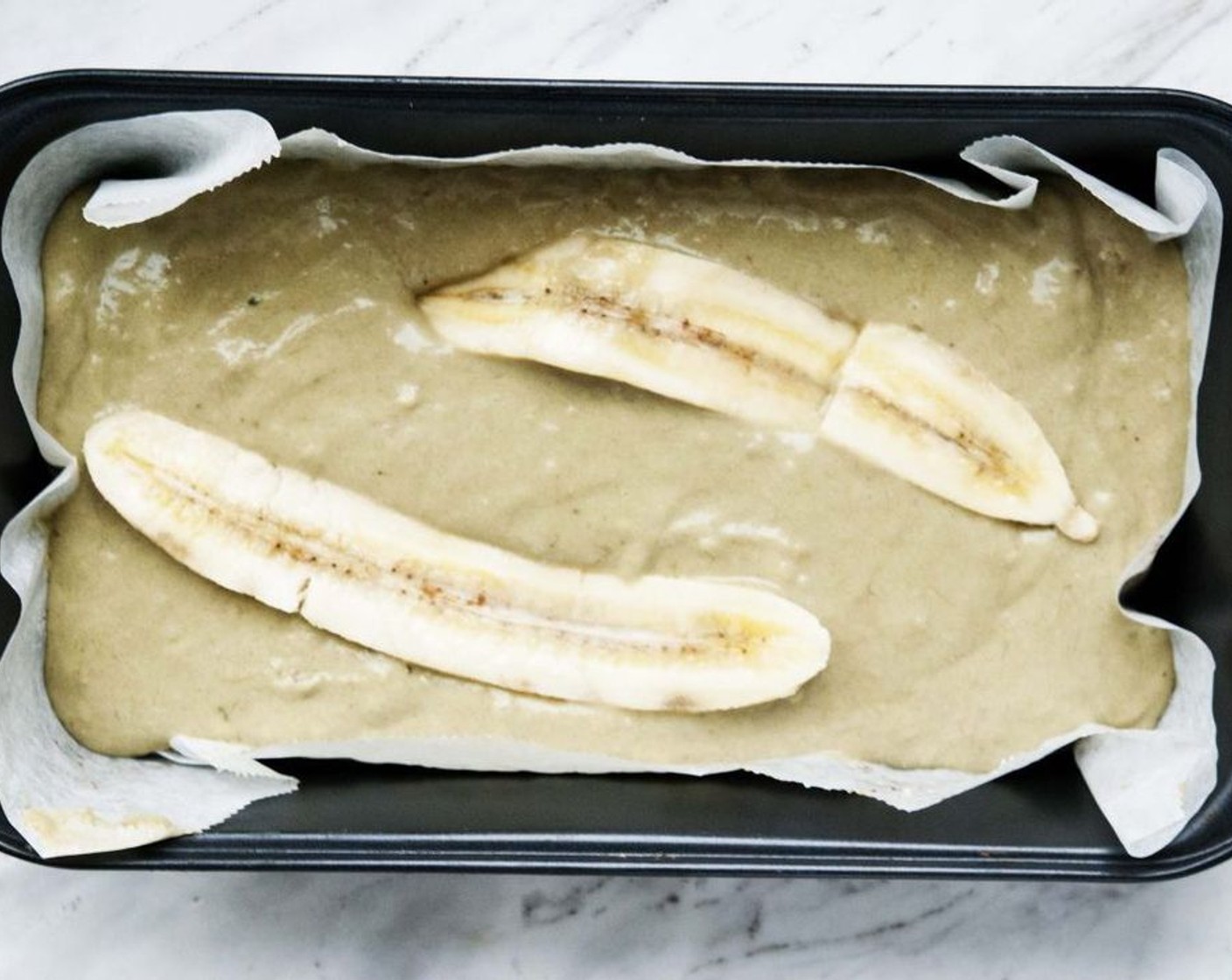 step 3 Line a bread loaf with parchment paper and pour in the batter. Slice up the 3rd Banana (1) lengthwise and lay it on top of the batter.