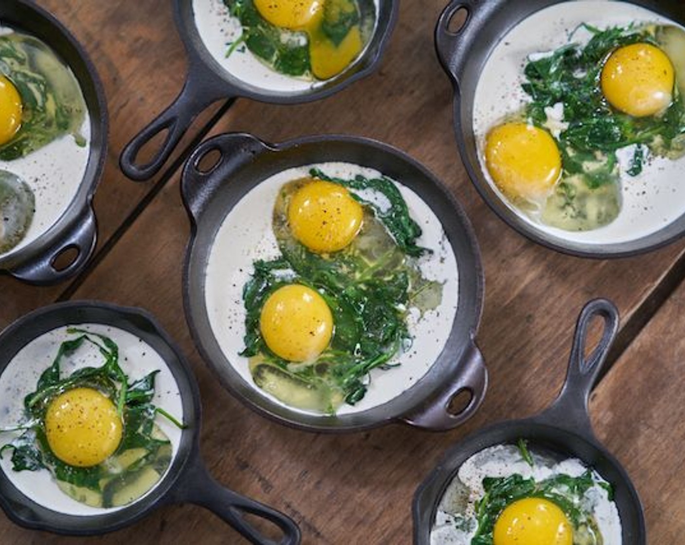 step 6 Create a small well in the spinach, and crack two Eggs (8) into each container. Season with Kosher Salt (to taste) and Freshly Ground Black Pepper (to taste).