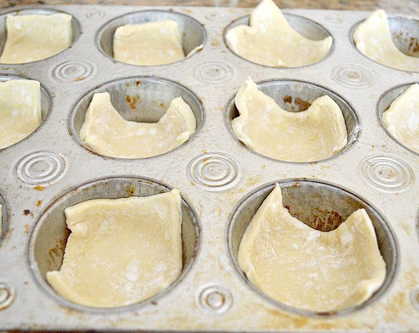 step 2 Take each sheet of Puff Pastry (2 sheets) and cut it into 12 squares. Do this by cutting along the fold seams to cut the sheet into thirds, then cut each third into 4 equal squares. Press each square into a muffin well to fill both tins.