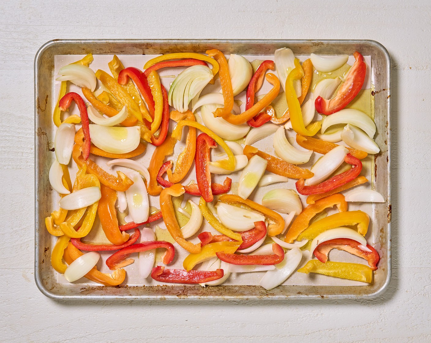 step 2 Arrange Assorted Color Bell Peppers (3) and Yellow Onions (2) on a parchment-lined sheet tray. Drizzle with olive oil and a pinch of salt.