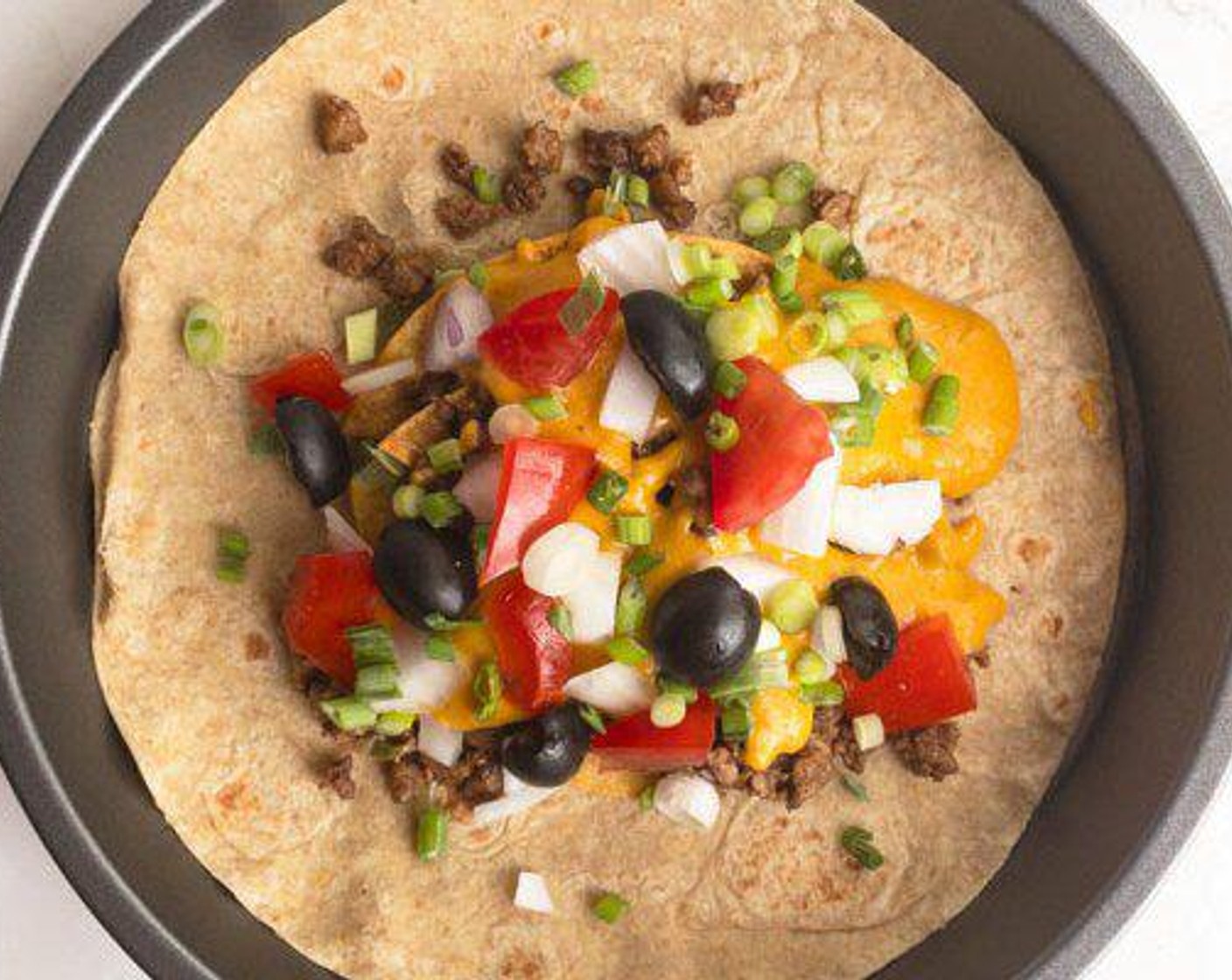 step 2 Add Vegan Ground Beef (1/2 cup), Tomato (1/4 cup), White Onion (1/4 cup), Fresh Chives (1 stalk), Black Olives (to taste), Vegan Nacho Cheese Sauce (1/2 cup) to the middle of the Whole Wheat Tortilla (1) and fold close as best you can.