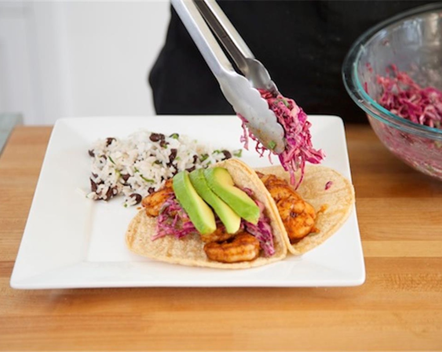 step 9 Place the rice evenly between two plates. Place two tortillas side by side on each plate with sides touching facing upwards. Place five shrimp on each tortilla in a single line. Top with slaw and then sliced avocado.