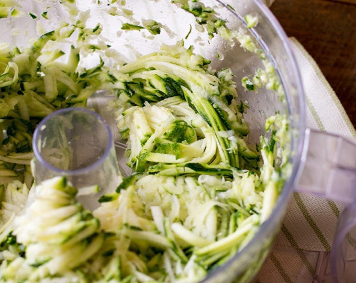 step 2 Grate Zucchini (2) with a food processor or by hand. Then place the zucchini in a colander and coat with a light layer of salt and wait 5-10 minutes. This helps sweat the water out of the zucchini.