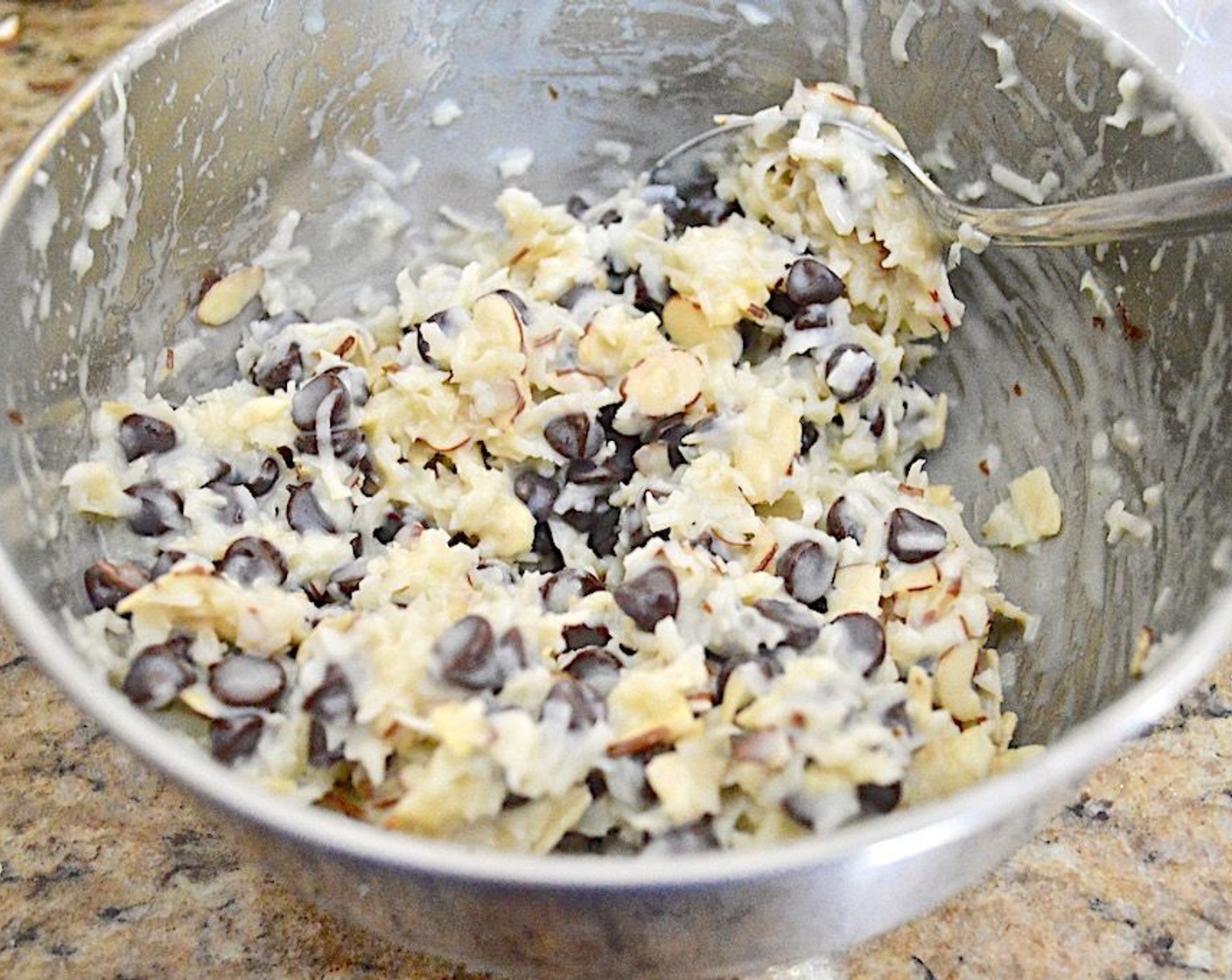 step 2 Combine the Unsweetened Coconut Flakes (1 1/2 cups), Semi-Sweet Chocolate Chips (1 cup), Sliced Almonds (1/2 cup), and Almond Extract (1/4 tsp) in a large mixing bowl and stir them together. Then pour in the Sweetened Condensed Milk (1 cup) and stir thoroughly so that the milk coats everything.