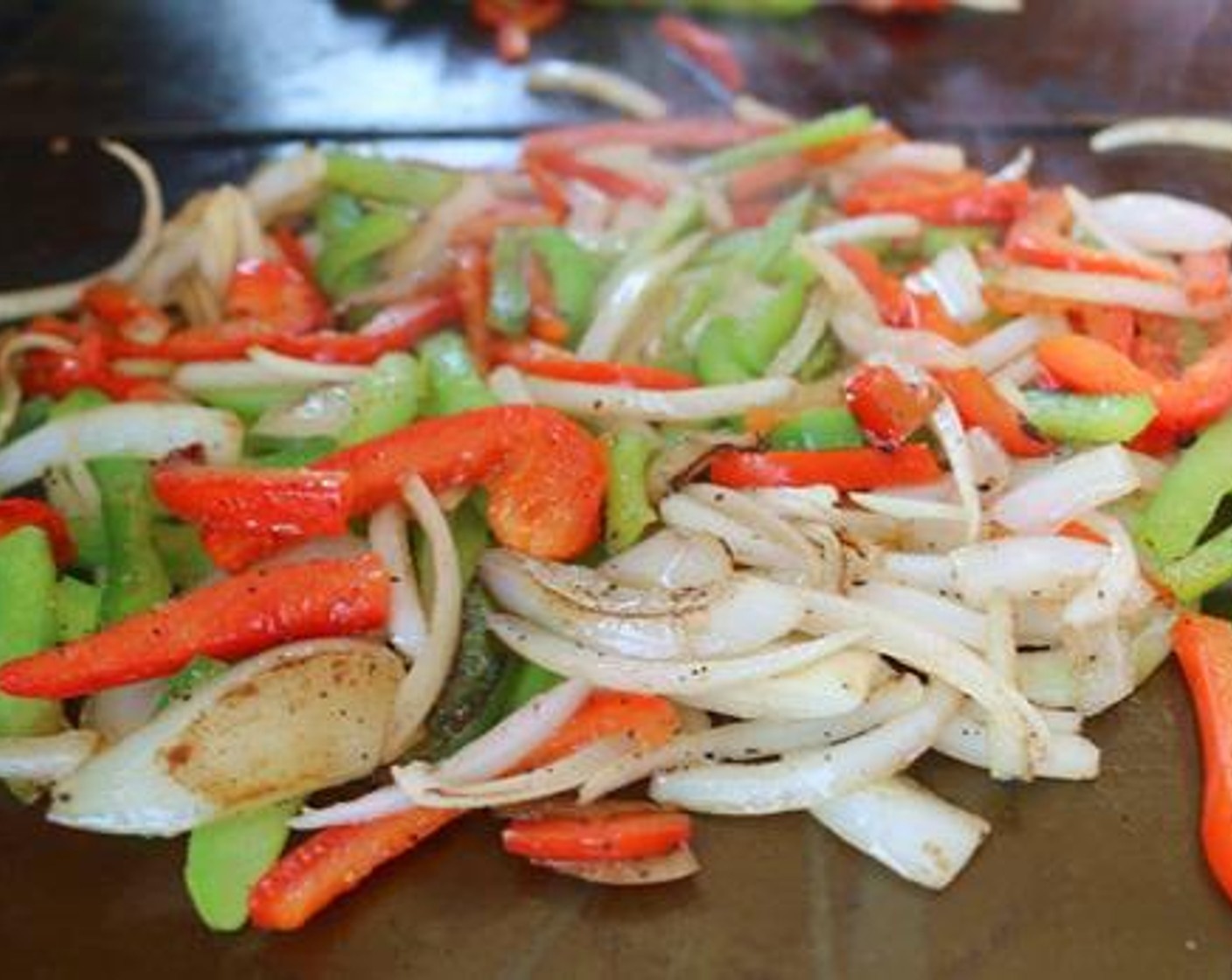 step 4 To make the Cheesesteaks , start with a little Cooking Oil (1/2 cup) on the griddle and add the Red Bell Pepper (1), Green Bell Pepper (1) and Onion (1). Season with a little Salt (to taste), Ground Black Pepper (to taste), and Garlic (1 clove), and sauté the veggies until tender.